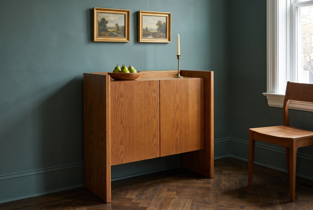 Trani oak veneer accent cabinet with a bowl of pears and a brass candlestick on its tray top, against a deep teal wall in a Philadelphia dining room with a herringbone floor