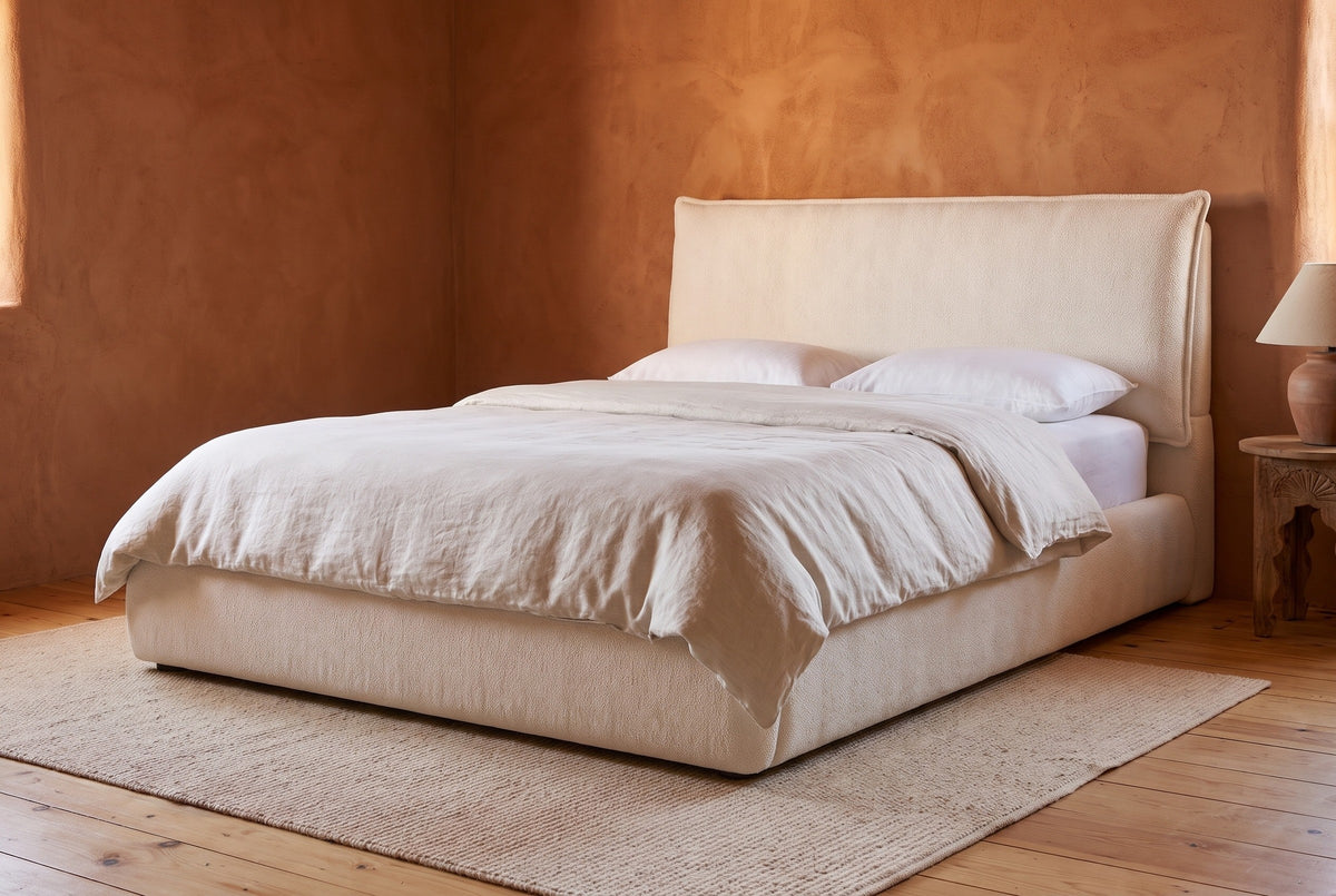 Trivento cream white chenille bed against a rust-orange clay plaster wall in a Santa Fe adobe bedroom with a pale pine floor and a wool rug
