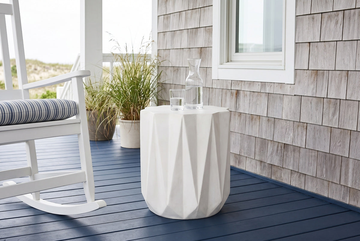 Troina antique white faceted concrete side table on a navy-painted porch floor against silver cedar shingles on the Outer Banks, beside a white rocking chair (chair and carafe not included)