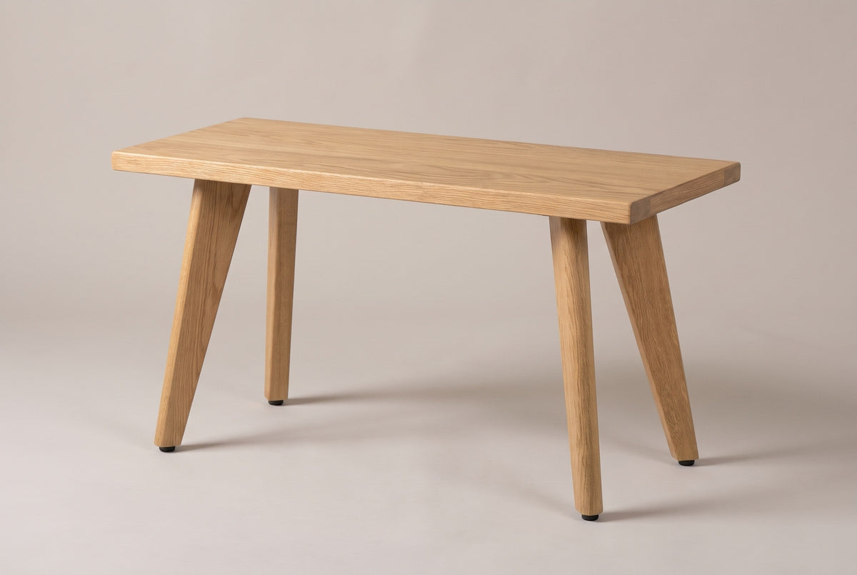 The Umbertide bench in natural red oak, three-quarter view on a light studio backdrop