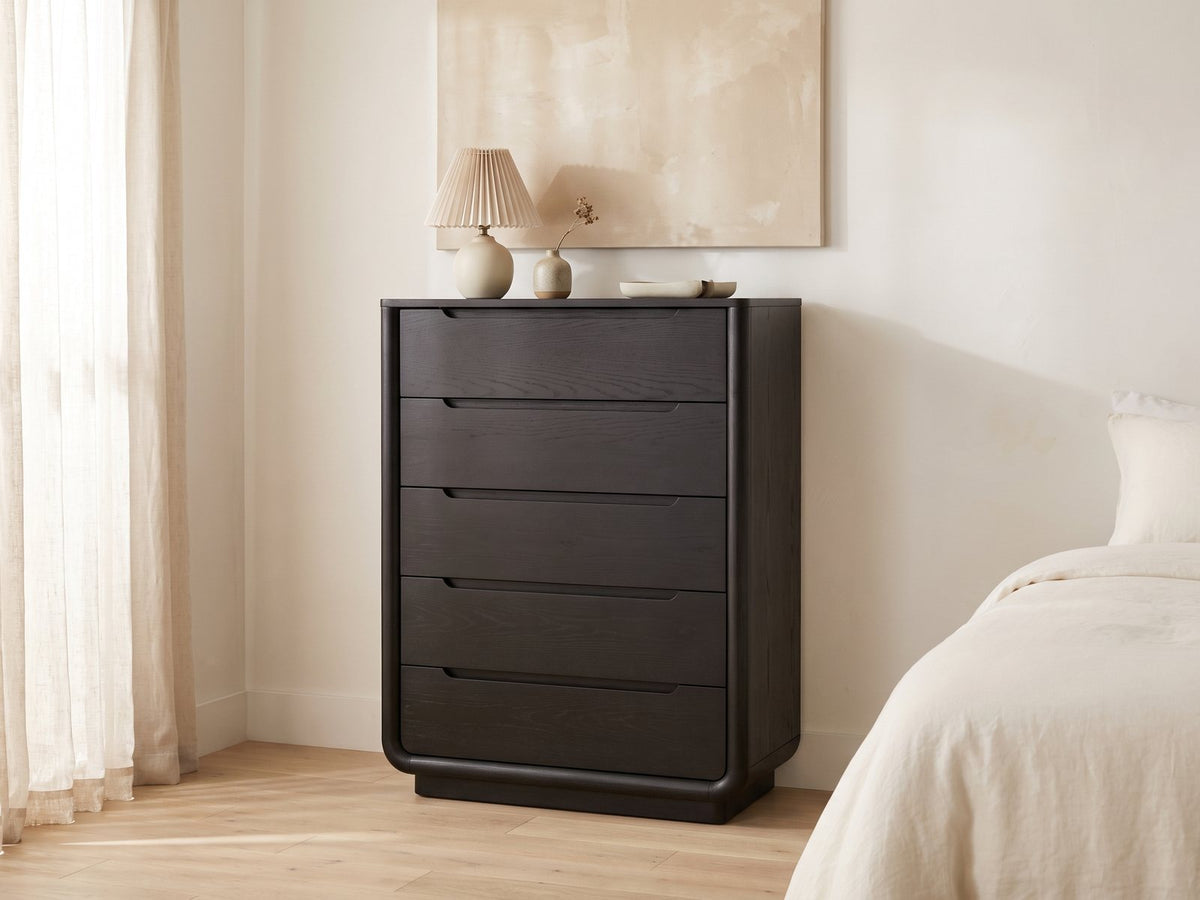 Valdobbiadene 40-Inch Burnished Black 5-Drawer Chest against a plaster wall under an abstract canvas in a bright bedroom