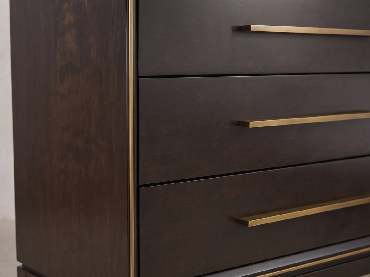 Close-up of the Valeggio 70-Inch Smoked Peppercorn 8-Drawer Dresser: the long antique-brass bar pulls and the thin brass band at the front corner