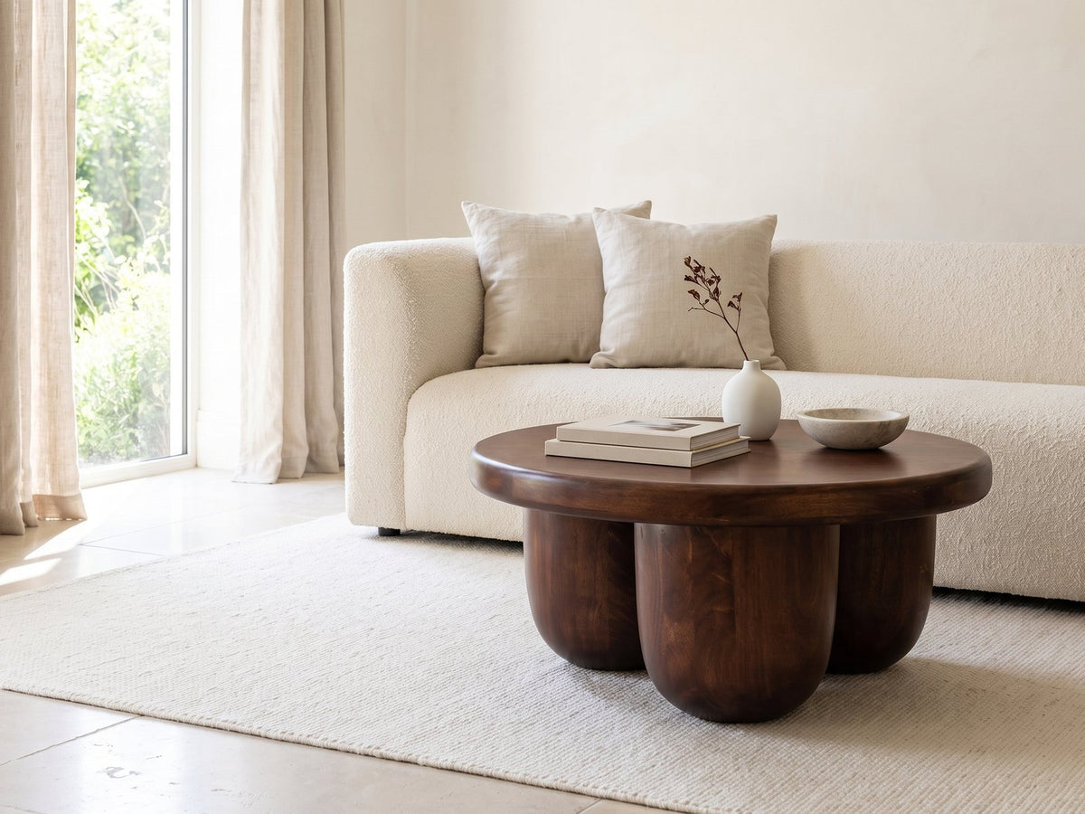Bolgheri Sculpted Mango Coffee Table styled with books, a vase and a stone bowl in front of a cream sofa in a bright plaster room
