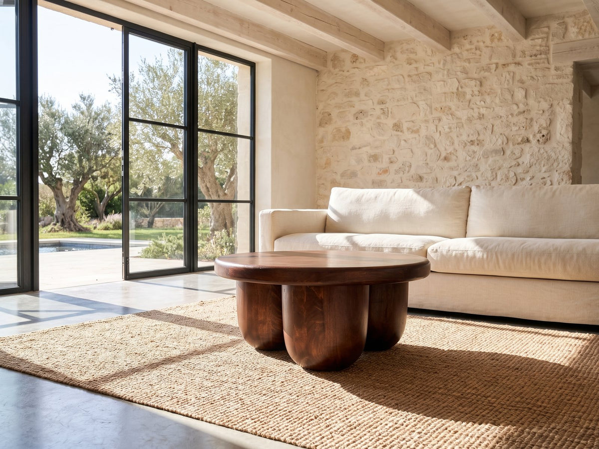 Bolgheri Sculpted Mango Coffee Table seen from the side, on a jute rug in front of a linen sofa in a poolside villa