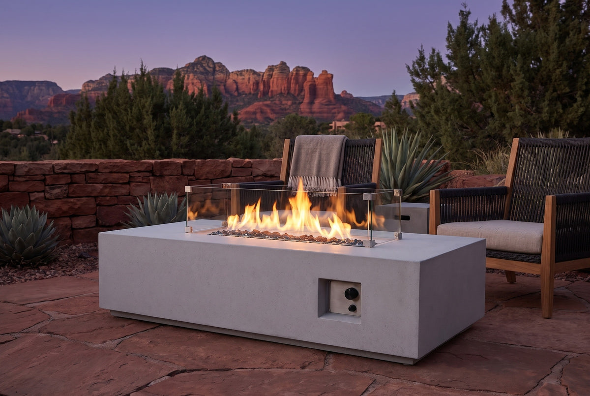 Vulcano concrete fire pit table lit at dusk on a red sandstone flagstone patio in Sedona, Arizona, with a dry-stacked red stone wall, agaves and red rock buttes behind (chairs not included)