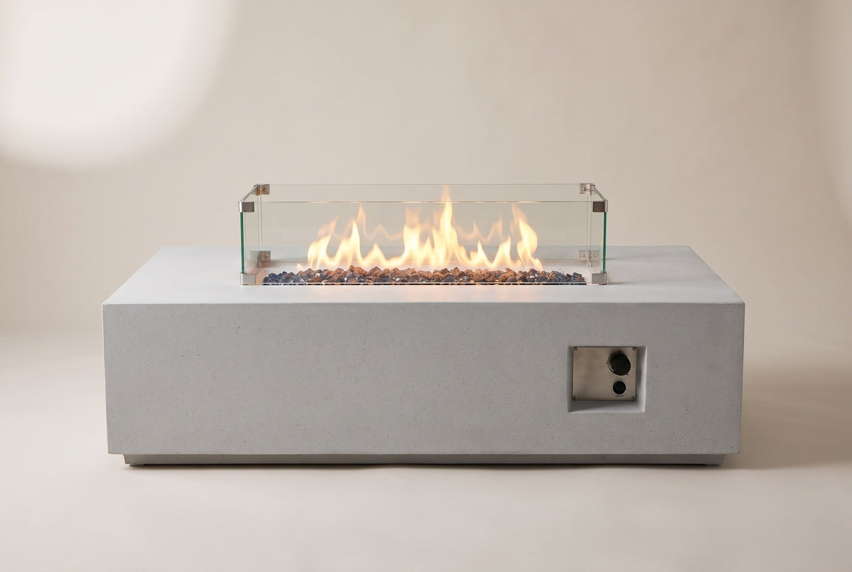 The Vulcano fire pit table seen from the front: the long concrete body, the glass wind guard with a lit flame and the control niche at the right-hand end