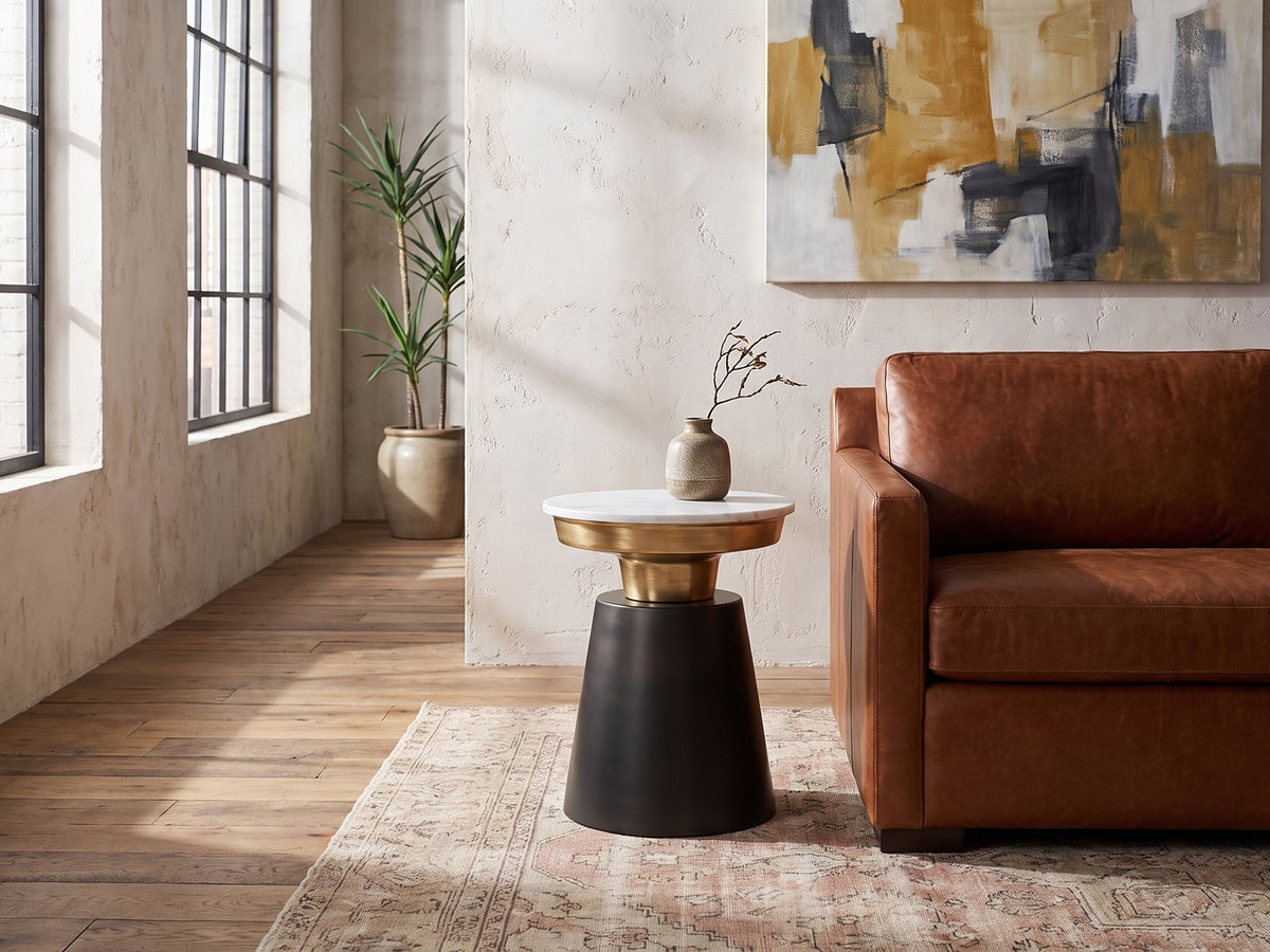 Acerenza White Marble Pedestal Side Table beside the arm of a cognac leather seat in an industrial loft