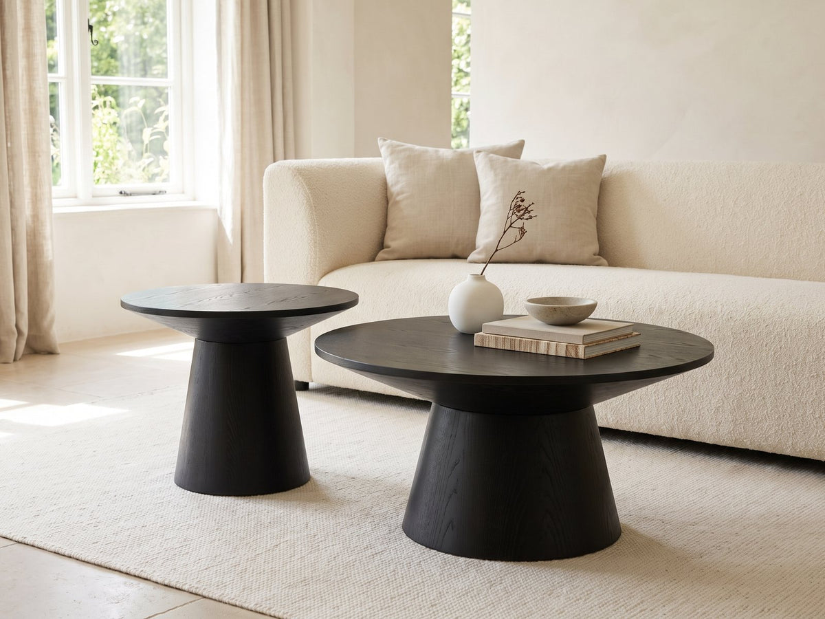 Acqui 29-Inch Round Ebony Oak Veneer Pedestal Coffee and End Table Set styled with books, a vase and a stone bowl in front of a cream sofa in a bright plaster room