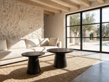 Acqui 29-Inch Round Ebony Oak Veneer Pedestal Coffee and End Table Set on a jute rug in front of a linen sofa in a poolside villa