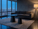 Acqui 29-Inch Round Ebony Oak Veneer Pedestal Coffee and End Table Set on a wool rug in front of a velvet sofa in a city penthouse at blue hour