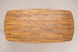 The Adrano dining table seen from directly above: the long top with rounded ends and six lengthwise acacia planks in a teak finish