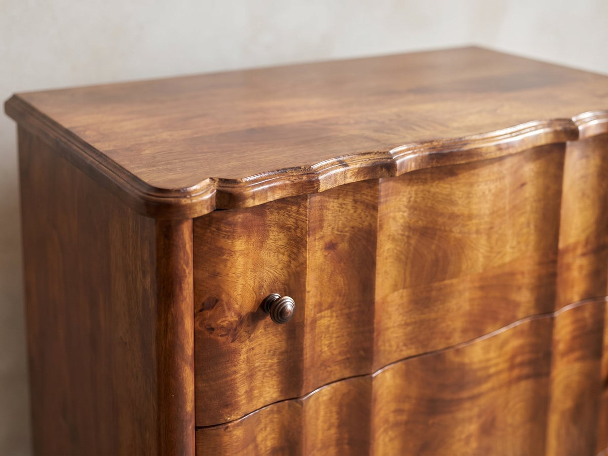 Close-up of the Adria 34-Inch Chestnut Solid Mango 3-Drawer Chest: the scalloped moulded top edge above the serpentine drawer fronts and their ringed knobs