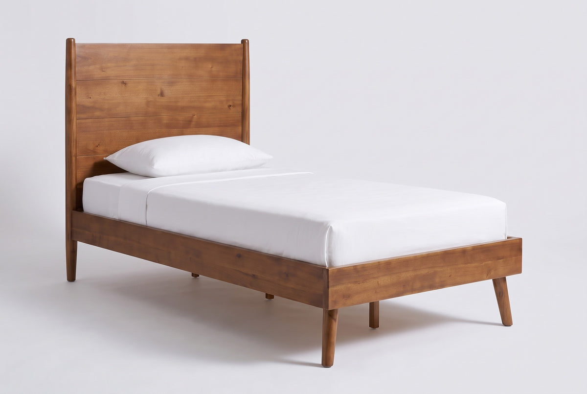 The Agnone bed in solid acacia with a board headboard, a white mattress and pillow (not included), three-quarter view on a light studio backdrop
