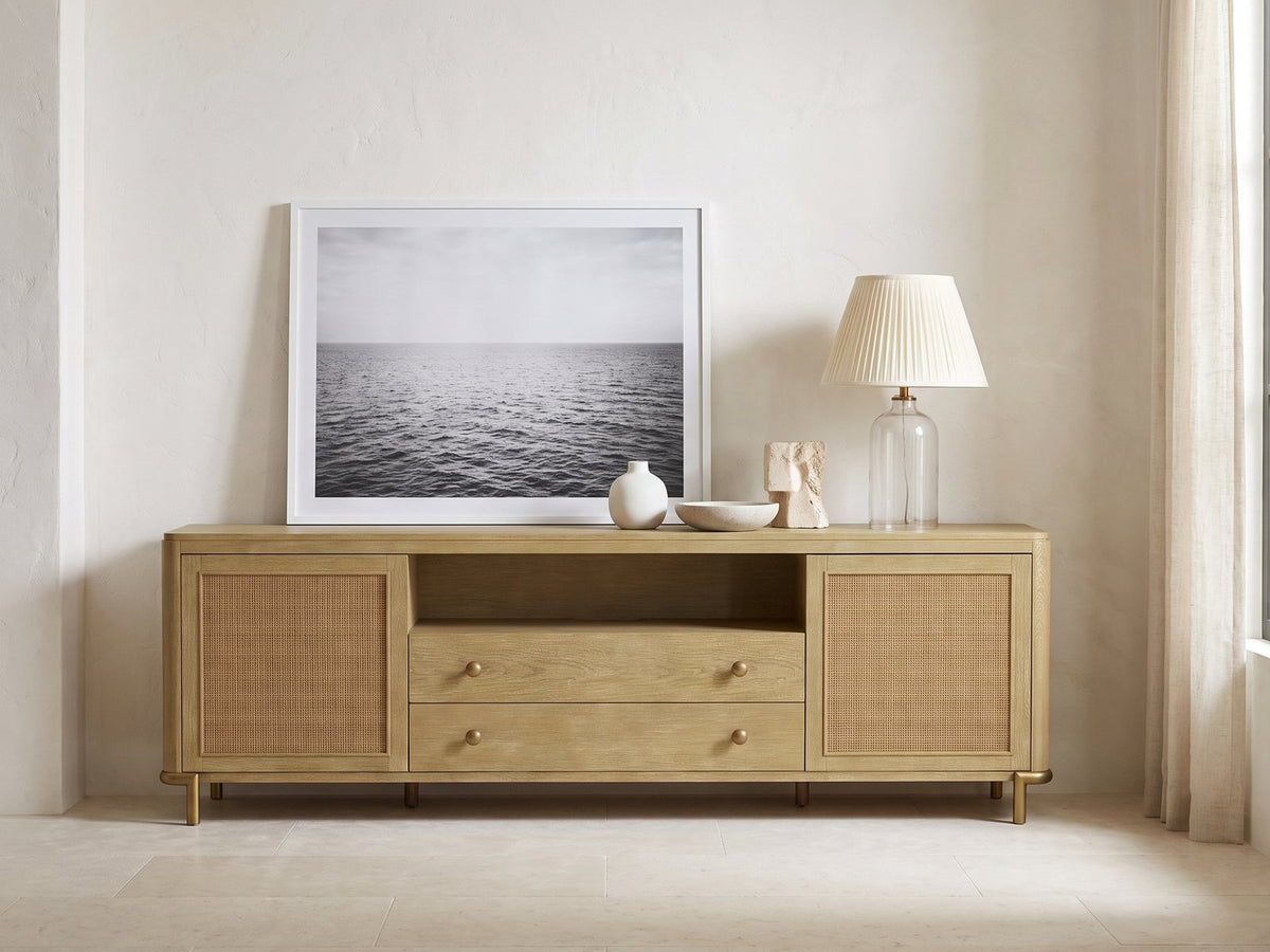 Alassio 80-Inch Sand Wash Ash and Rattan Media Console styled with a leaning print, a lamp and ceramics in a bright plaster room