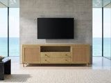 Alassio 80-Inch Sand Wash Ash and Rattan Media Console under a wall-mounted screen in an oceanfront glass house