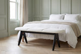 Alatri white fabric bench at the foot of a made bed with white linen bedding in a Boston bedroom with sage-green panelled walls and a herringbone oak floor (bed and bedding not included)