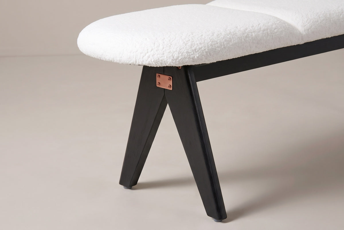 One end of the Alatri bench: the rounded end of the white fabric seat, a rail beneath it, a small copper-tone plate with four screws at the joint, and two flat black legs spreading apart below