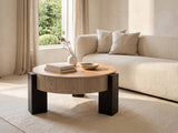 Alba 31.5-Inch Round Parquet Wood Veneer Storage Coffee Table seen from the side, styled with books, a vase and a stone bowl in front of a cream sofa in a bright plaster room