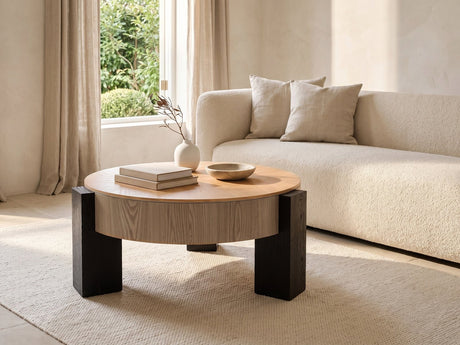 Alba 31.5-Inch Round Parquet Wood Veneer Storage Coffee Table seen from the side, styled with books, a vase and a stone bowl in front of a cream sofa in a bright plaster room