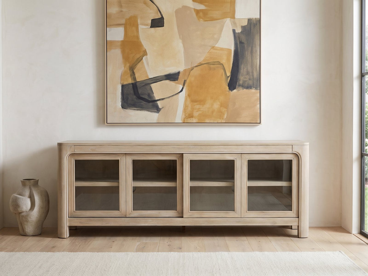 Albenga 71-Inch Weathered Mango Veneer Sliding Glass Door Media Console under a large abstract painting in a bright living room