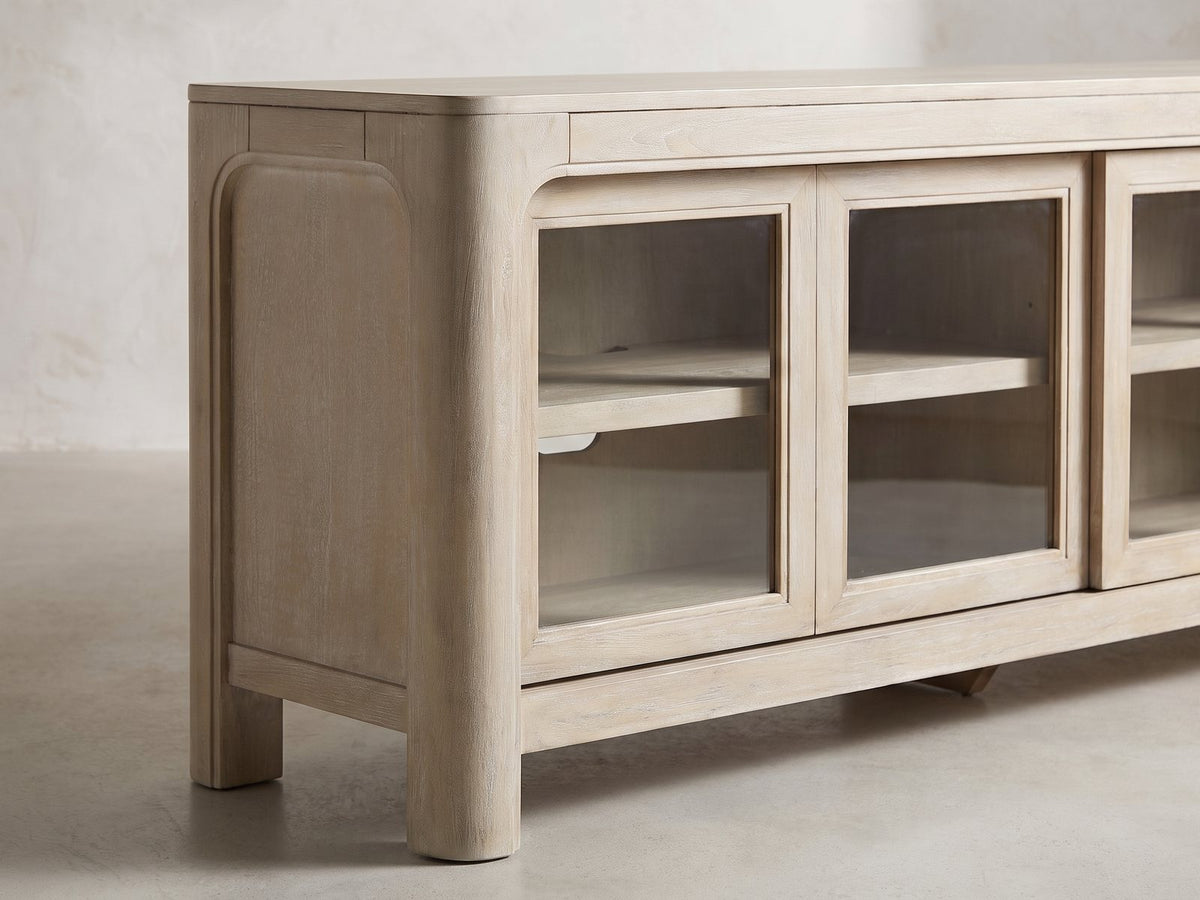 Close-up of the Albenga 71-Inch Weathered Mango Veneer Sliding Glass Door Media Console: the rounded bullnose corner, arched end panel and rounded leg in weathered mango