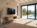 Alberobello Low Mango Media Console seen from the side, under a wall-mounted screen on a pale stone wall in a poolside villa