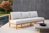 The Alcamo armless acacia sofa by a long pool on a Houston limestone terrace, a charcoal board-formed concrete wall and a pink crepe myrtle behind (coffee table not included)