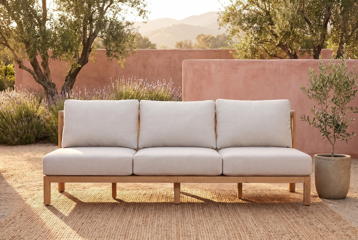 The Alcamo armless acacia sofa on a jute rug in front of a pink lime-washed adobe wall on a garden terrace in Ojai, olive trees and lavender behind (rug and planter not included)