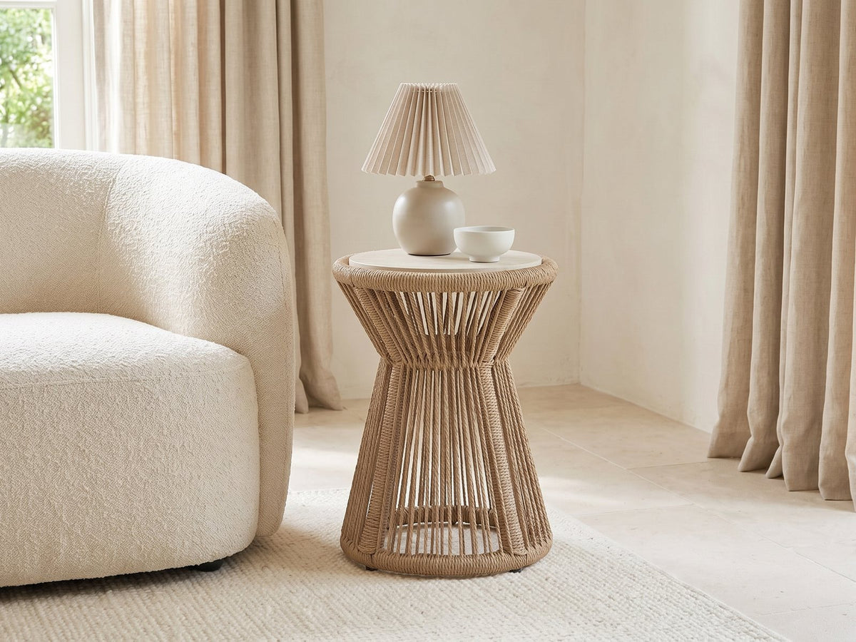 Alessano Rope Hourglass Side Table with a lamp and a ceramic bowl beside a cream boucle armchair in a bright plaster room