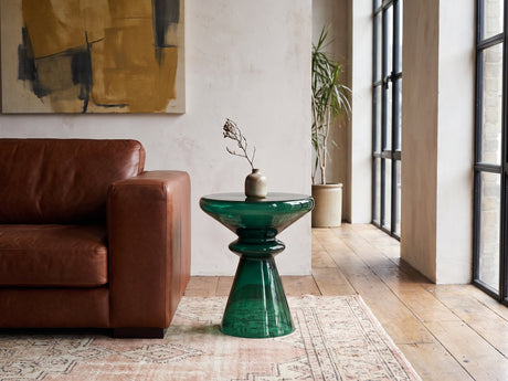 Alliste Blown Glass Hourglass Side Table beside a leather sofa in an industrial loft