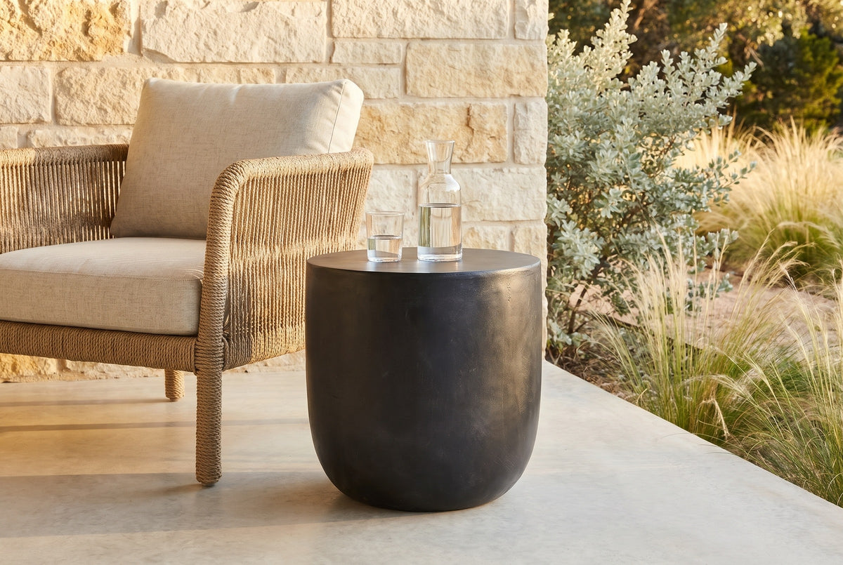Altavilla matte black concrete side table on a pale concrete porch in Austin, a limestone wall, a rope lounge chair and Texas sage behind (chair and carafe not included)