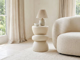 Altomonte Cream Fiberglass Stacked Side Table with a lamp and a ceramic bowl beside a cream boucle armchair in a bright plaster room