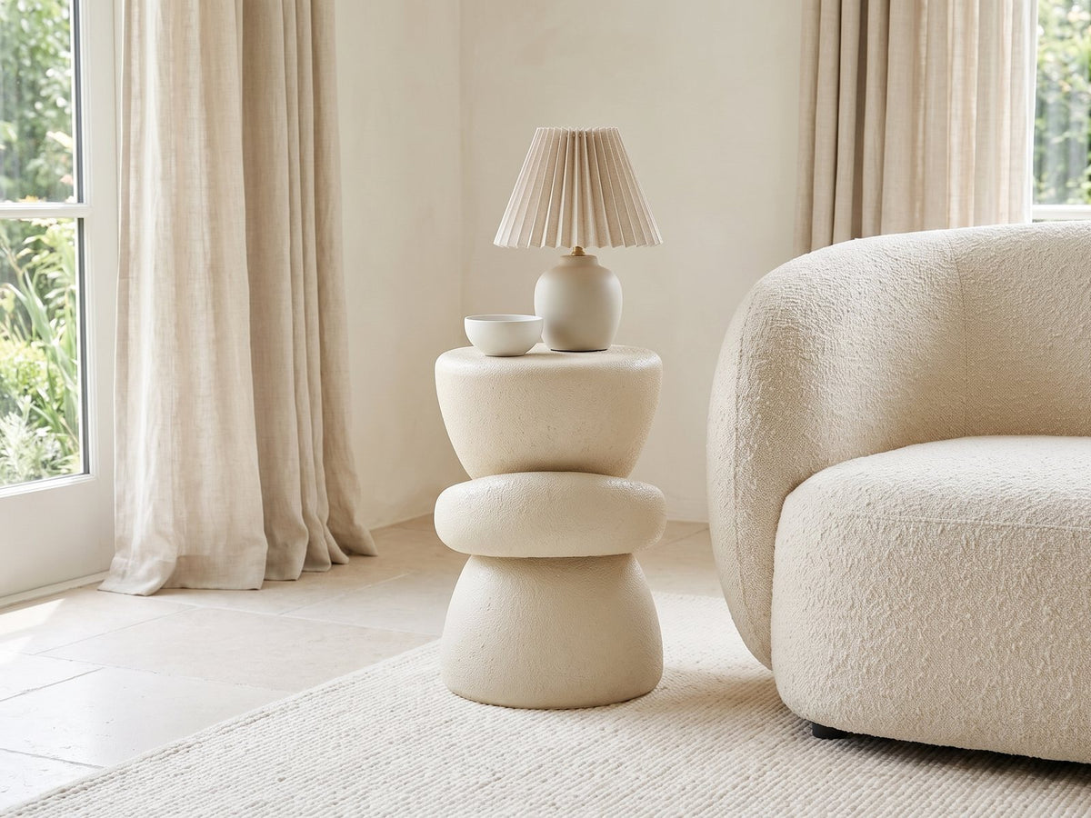 Altomonte Cream Fiberglass Stacked Side Table with a lamp and a ceramic bowl beside a cream boucle armchair in a bright plaster room