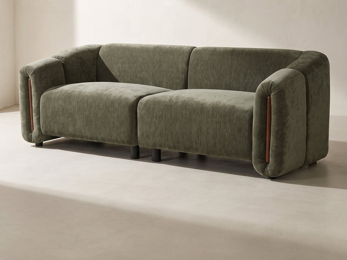 Amalfi Curved Sofa in olive green against a plaster wall in morning light