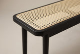 One end of the Anagni bench: the rounded corner of the black oak frame, the thin cane binding and the cane seat, above the slim apron and the round legs