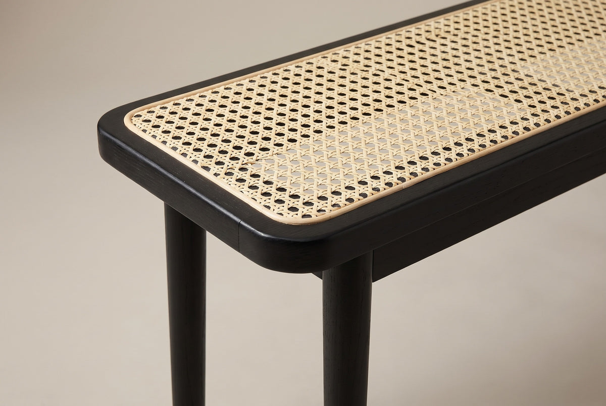 One end of the Anagni bench: the rounded corner of the black oak frame, the thin cane binding and the cane seat, above the slim apron and the round legs