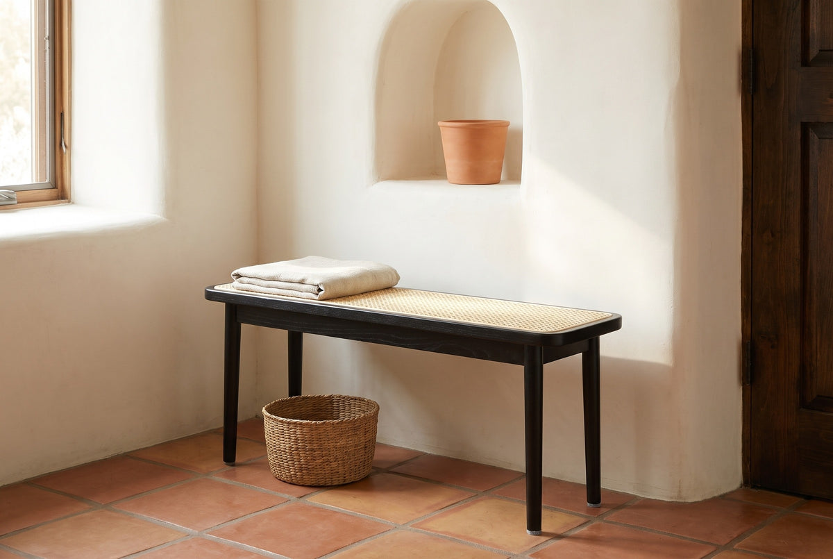 Anagni bench with a folded linen throw against a white adobe plaster wall with an arched niche in a Santa Fe entry hall, with a terracotta tile floor and a seagrass basket