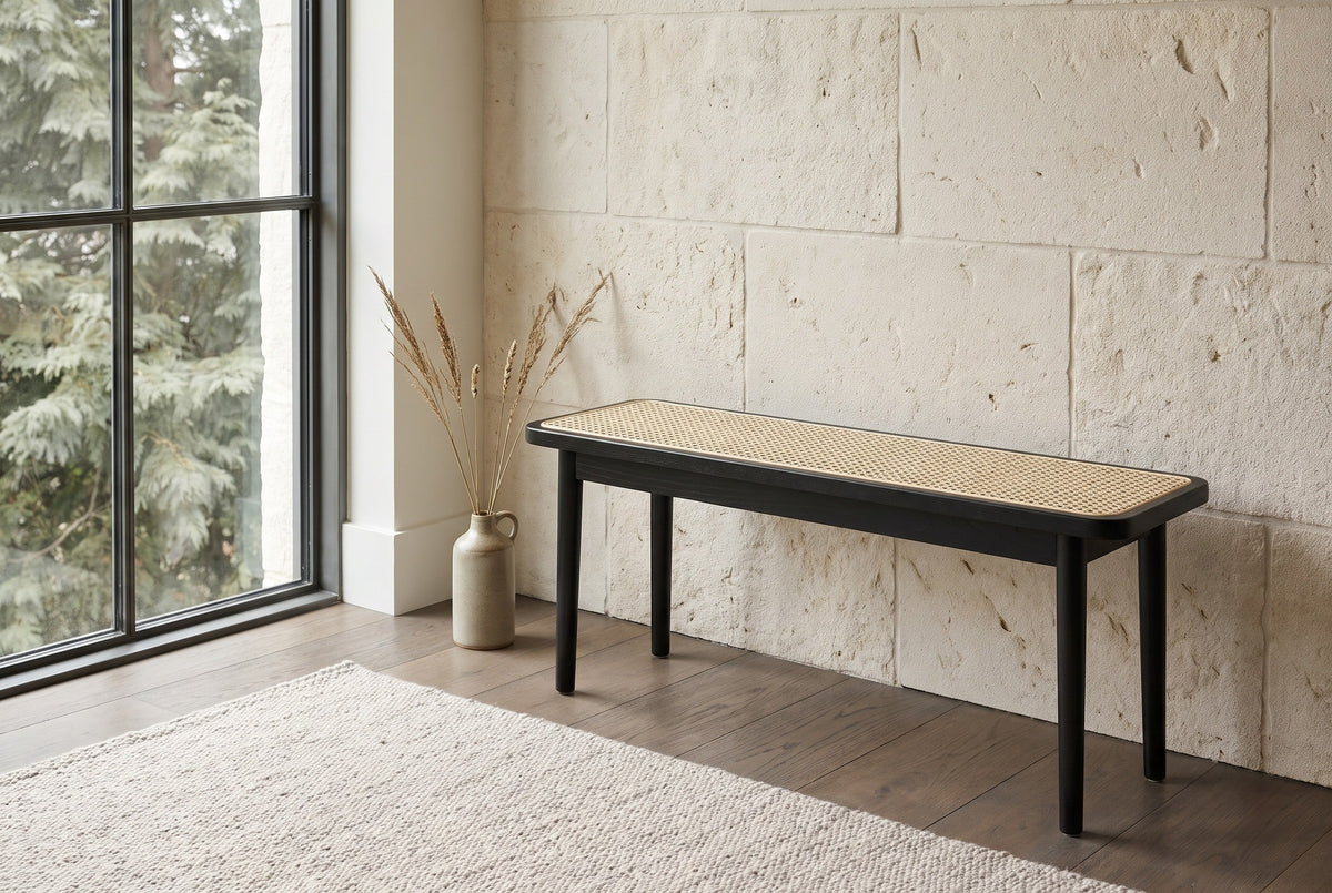Anagni black oak cane bench against a pale limestone block wall in a Seattle living room with a steel-framed window, a smoked oak floor and a vase of dried grasses