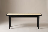 The Anagni bench in black oak with a natural cane seat, side view on a light studio backdrop