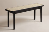 The Anagni bench in black oak with a natural cane seat, three-quarter view on a light studio backdrop