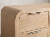 Close-up of the Aquileia 63-Inch Natural Mango 9-Drawer Dresser: a slim pewter finger pull on the top edge of a drawer, beside the rounded waterfall corner