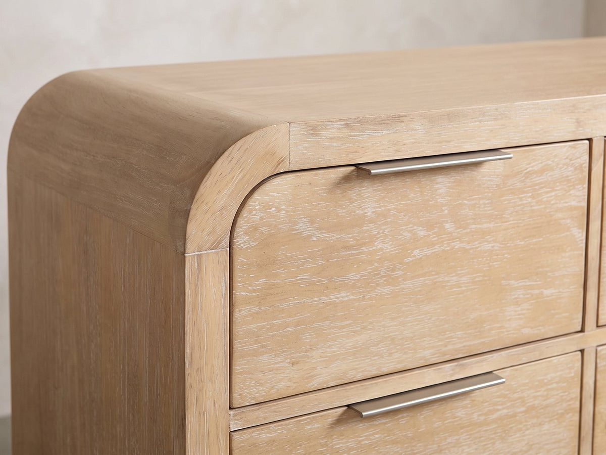 Close-up of the Aquileia 63-Inch Natural Mango 9-Drawer Dresser: a slim pewter finger pull on the top edge of a drawer, beside the rounded waterfall corner