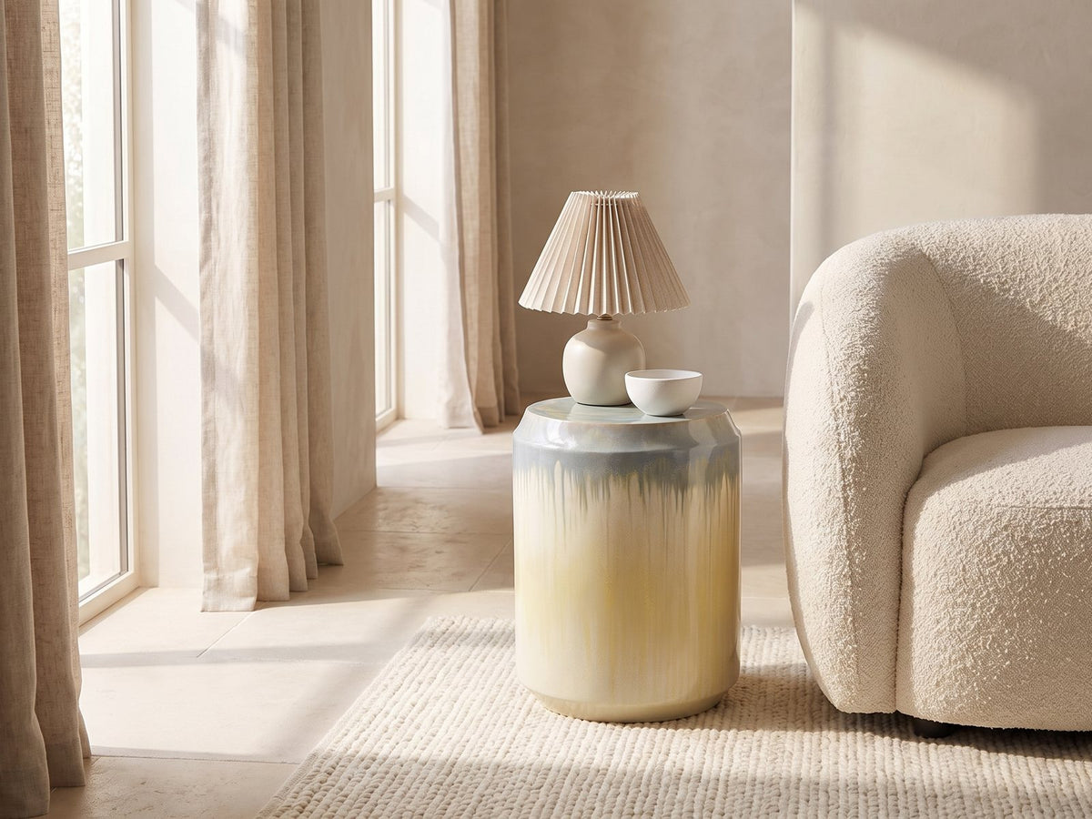 Aradeo Reactive Glaze Ceramic Drum Side Table with a lamp and a ceramic bowl beside a cream boucle armchair in a bright plaster room