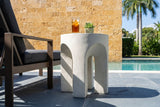 Aragona antique white arched side table with iced tea and a succulent beside a bronze lounge chair on a bluestone pool terrace in Coral Gables, a coral stone wall behind (chair and decor not included)