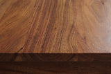 Close-up of the walnut-brown acacia on the Arborea nightstand: bold flowing grain with golden highlights running to a square edge
