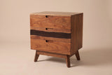 The Arborea three-drawer nightstand in walnut-brown acacia with a dark band across the middle drawer, three-quarter view on a light studio backdrop