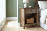 Arbus aged brown one-drawer nightstand with a ceramic lamp and a seagrass basket beside a bed in a Minneapolis bedroom with a moss-green wall