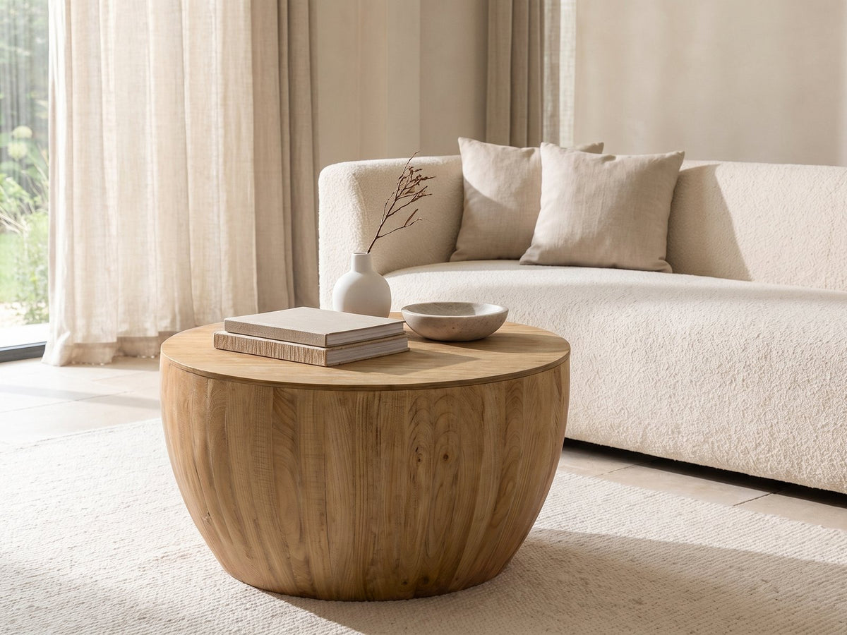 Arona 31.5-Inch Round Solid Fir Storage Drum Coffee Table styled with books, a vase and a stone bowl in front of a cream sofa in a bright plaster room