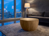 Arona 31.5-Inch Round Solid Fir Storage Drum Coffee Table on a wool rug in front of a velvet sofa in a city penthouse at blue hour