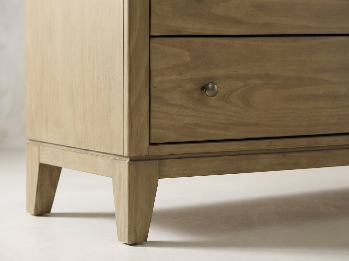 Close-up of the Arqua 61-Inch Natural Pine 8-Drawer Dresser: the apron and a square tapered leg at the front corner